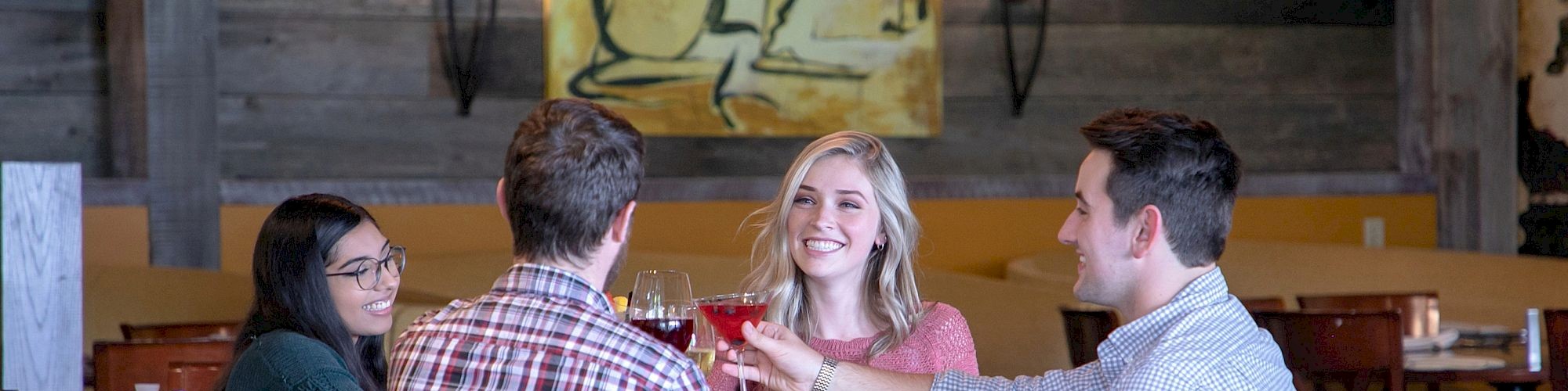 Four people are sitting at a restaurant table, engaging in conversation and raising their glasses for a toast.