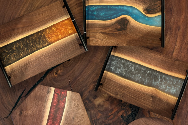 The image shows several wood and resin trays with vibrant river-like patterns in blue, orange, red, and gray shades arranged on a wooden surface.