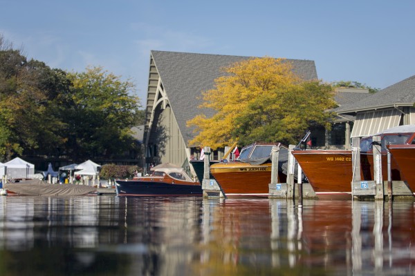 The image shows a waterfront scene with wooden boats docked, a building with a peaked roof, trees, and tents in the background ending the sentence.