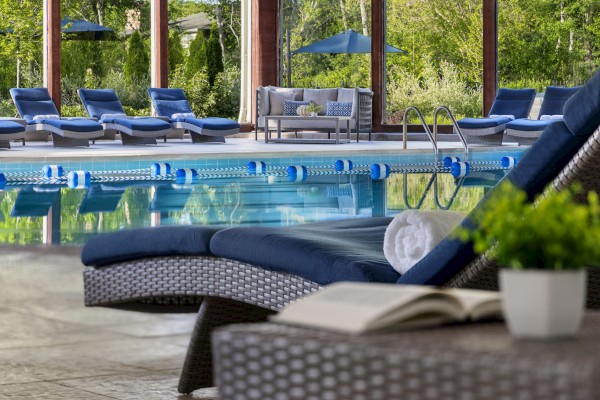 A serene indoor pool setting with chaise lounges, a rolled towel, open book, and potted plant, offering a relaxing atmosphere.