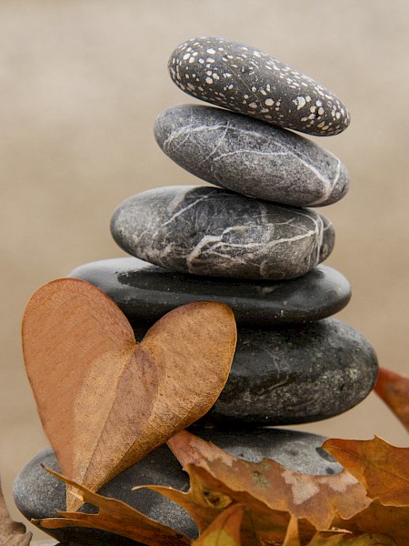 A stack of smooth stones with a heart-shaped leaf and dry leaves surrounding them, creating a serene and natural composition.