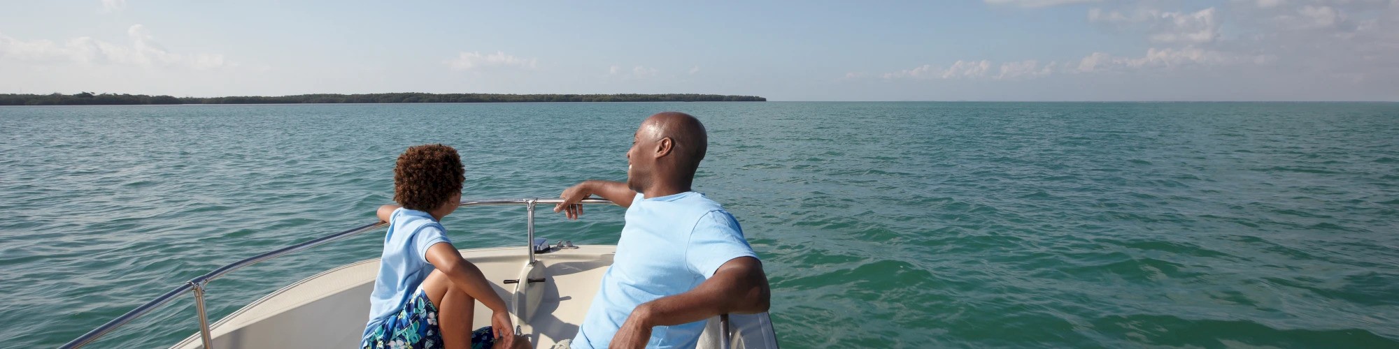 Two people are sitting on a boat, enjoying the expansive view of the calm sea under a clear sky.