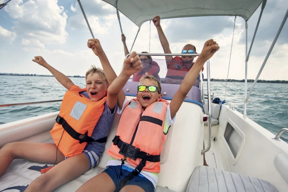 People are on a boat wearing life jackets, cheering with raised arms and enjoying the ride on the water.