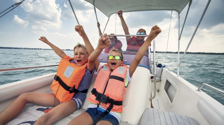 People are on a boat wearing life jackets, cheering with raised arms and enjoying the ride on the water.