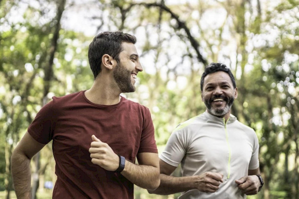 Two people are jogging and smiling in a wooded outdoor area, enjoying the fresh air and greenery around them.