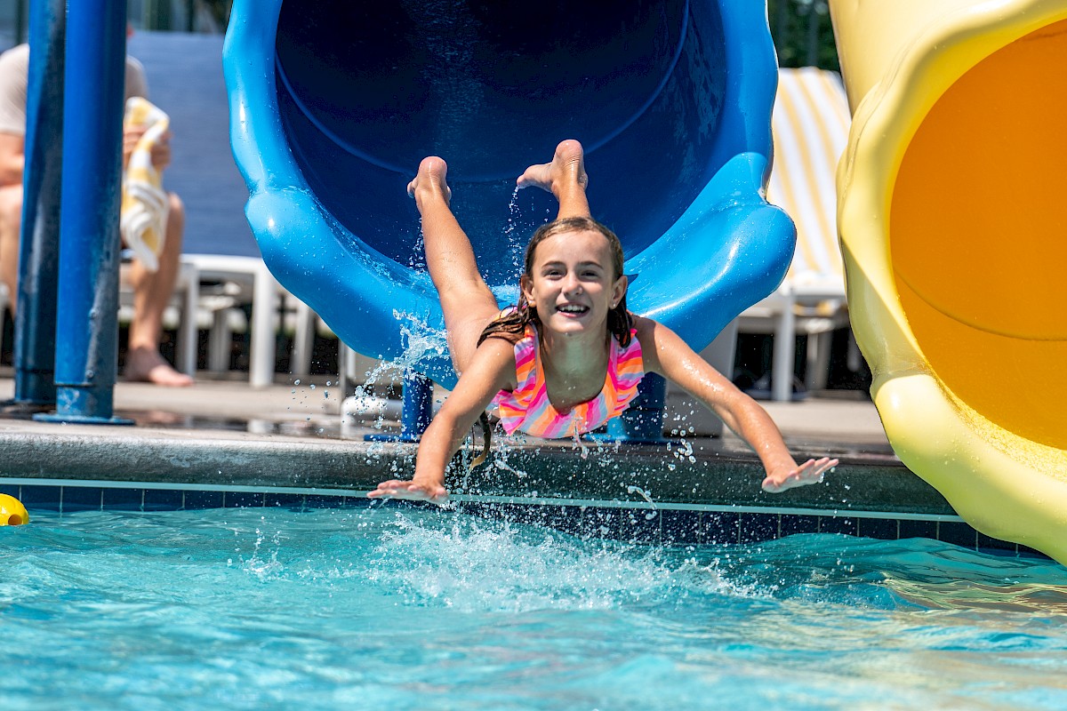 A person is emerging from a blue water slide into a pool, with others swimming nearby.