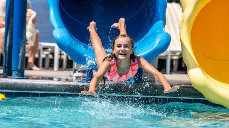 A person is emerging from a blue water slide into a pool, with others swimming nearby.