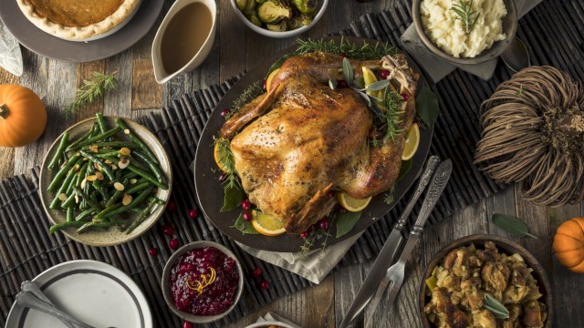 A table is set with a roasted turkey, mashed potatoes, green beans, stuffing, cranberry sauce, sweet potatoes, gravy, pie, and various vegetables.
