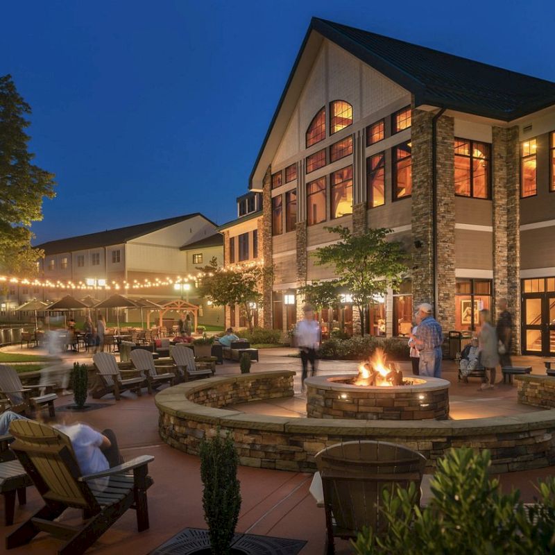 An outdoor fireside seating area at a large, well-lit building with string lights and people enjoying a relaxed evening setting.
