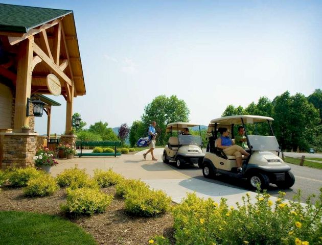 The image shows a golf course entrance with two golf carts and three people. Flower beds and a wooden building feature prominently in the scene.