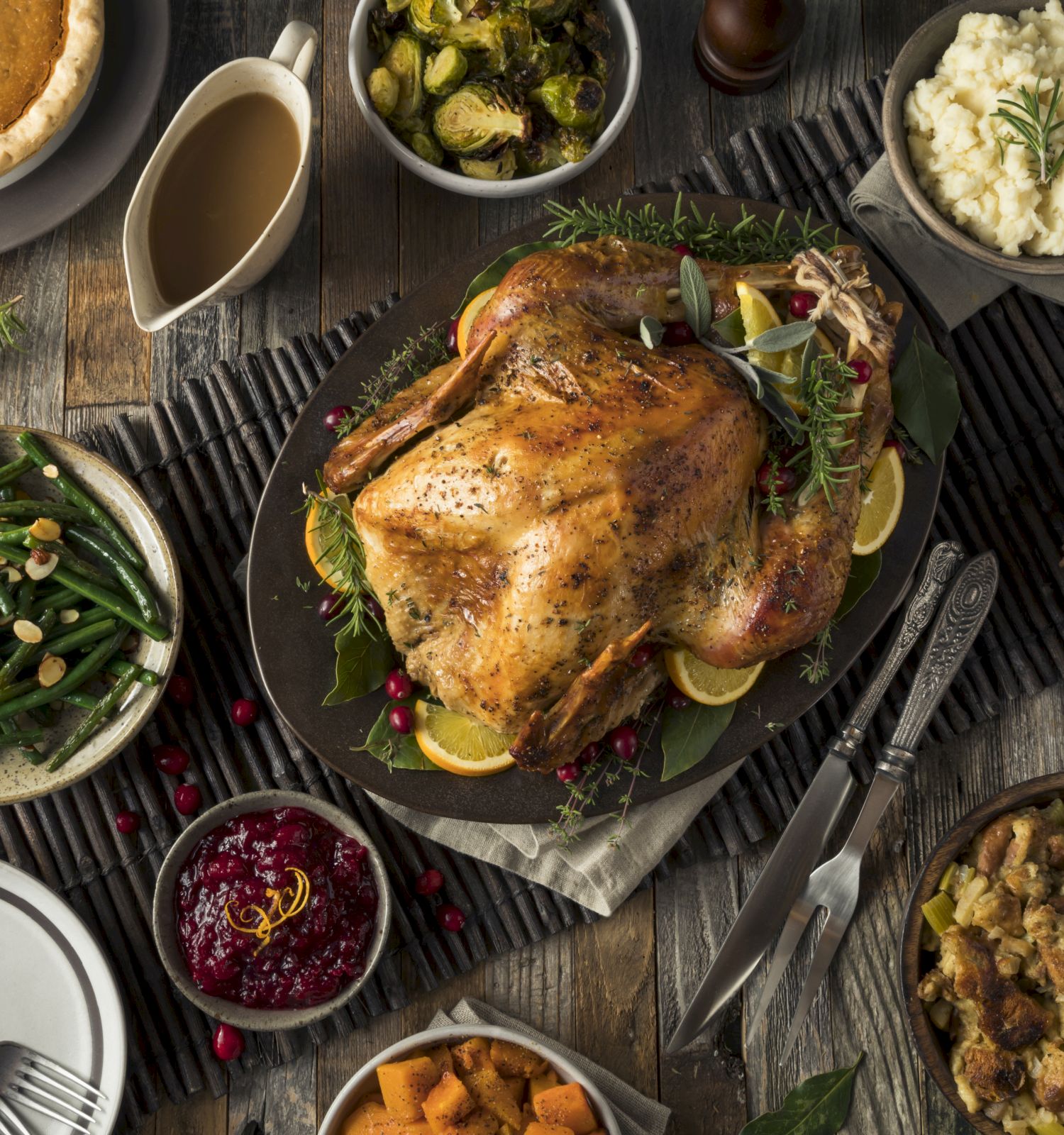 A Thanksgiving meal with roasted turkey, green beans, mashed potatoes, stuffing, pie, gravy, cranberries, sweet potatoes, Brussels sprouts, and pumpkins.